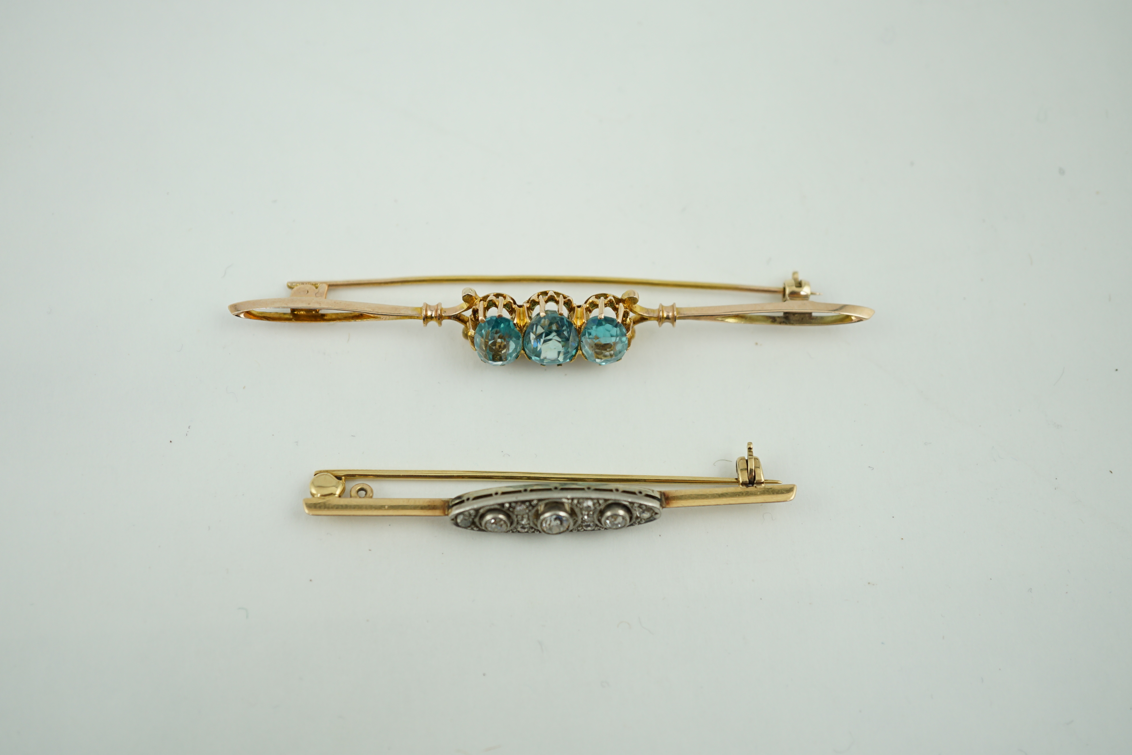 A 1920's yellow metal and millegrain diamond cluster set bar brooch, 56mm, together with a yellow metal and three stone blue zircon set bar brooch